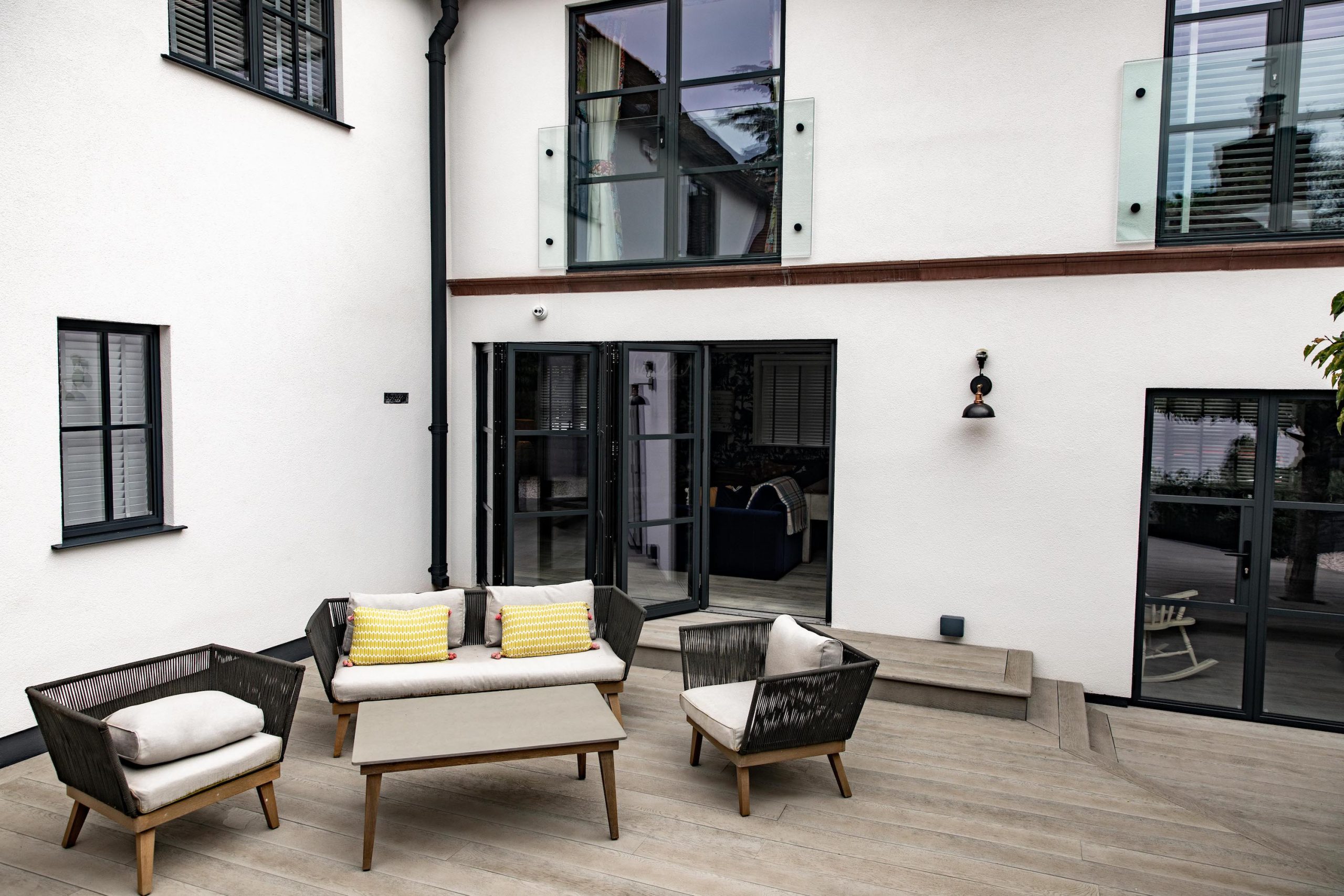 Garden sofas and chairs are shown against glass windows and doors are shown in the white walls of Woodbrook Place, Cheshire.