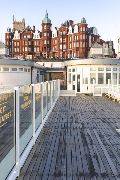 The glass panels are shown running along a pier, with white frames, with a view onto the land and Norfolk skyline. 